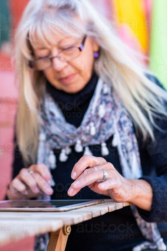 Mature lady wearing spectacles using tablet - Australian Stock Image