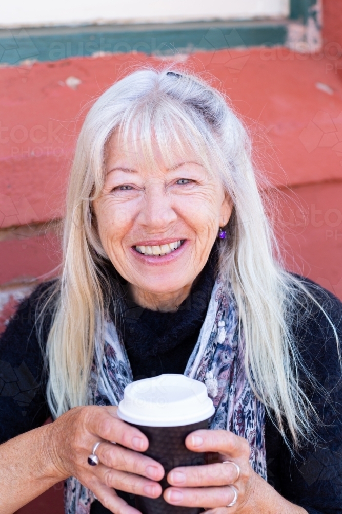 mature lady with long hair holding takeaway coffee cup with both hands - Australian Stock Image