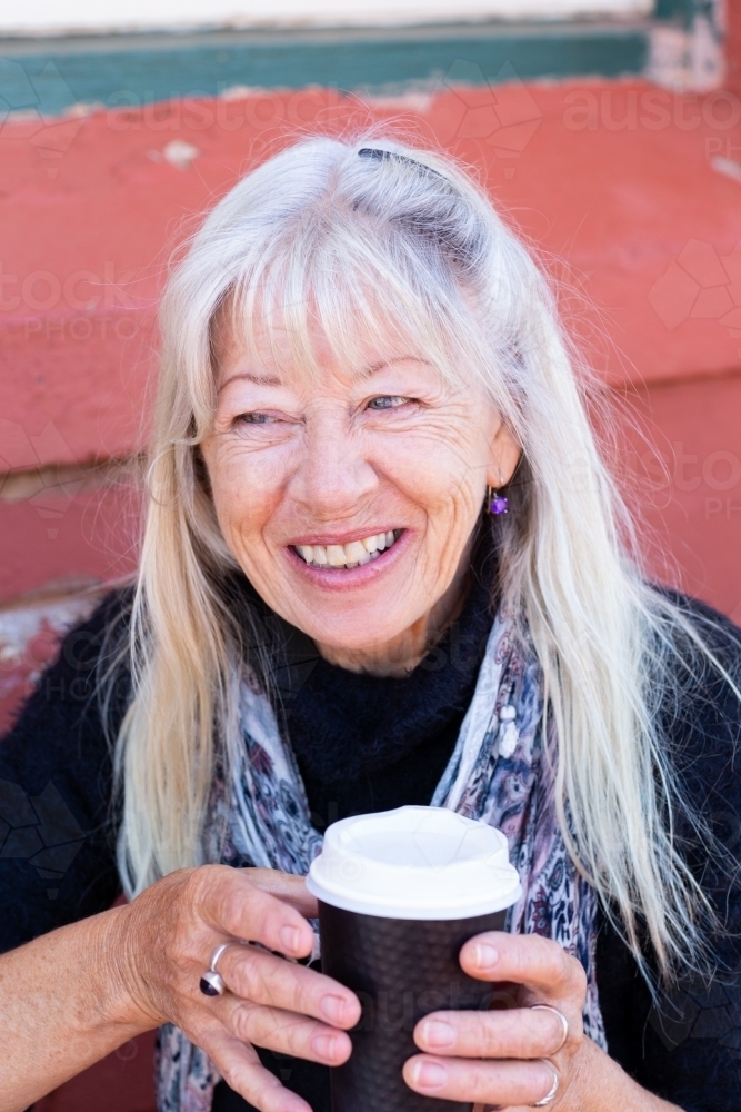 mature lady with long hair holding takeaway coffee cup with both hands - Australian Stock Image