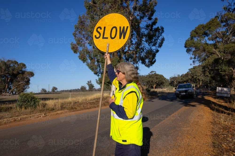 mature lady with slow and stop sign managing traffic on road - Australian Stock Image