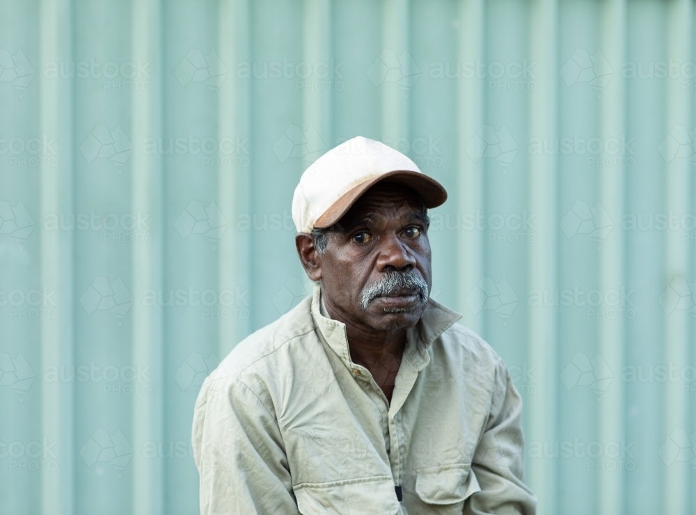 Mature man wearing cap against a metal fence - Australian Stock Image