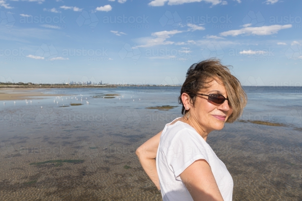 Mature middle eastern woman surveying tidal shallows - Australian Stock Image
