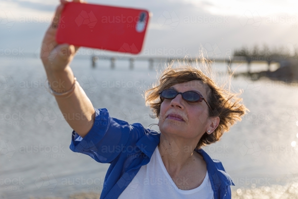 Mature middle eastern woman taking selfie on beach - Australian Stock Image