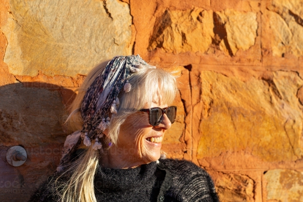 Mature woman head and shoulders against sunlit stone wall - Australian Stock Image
