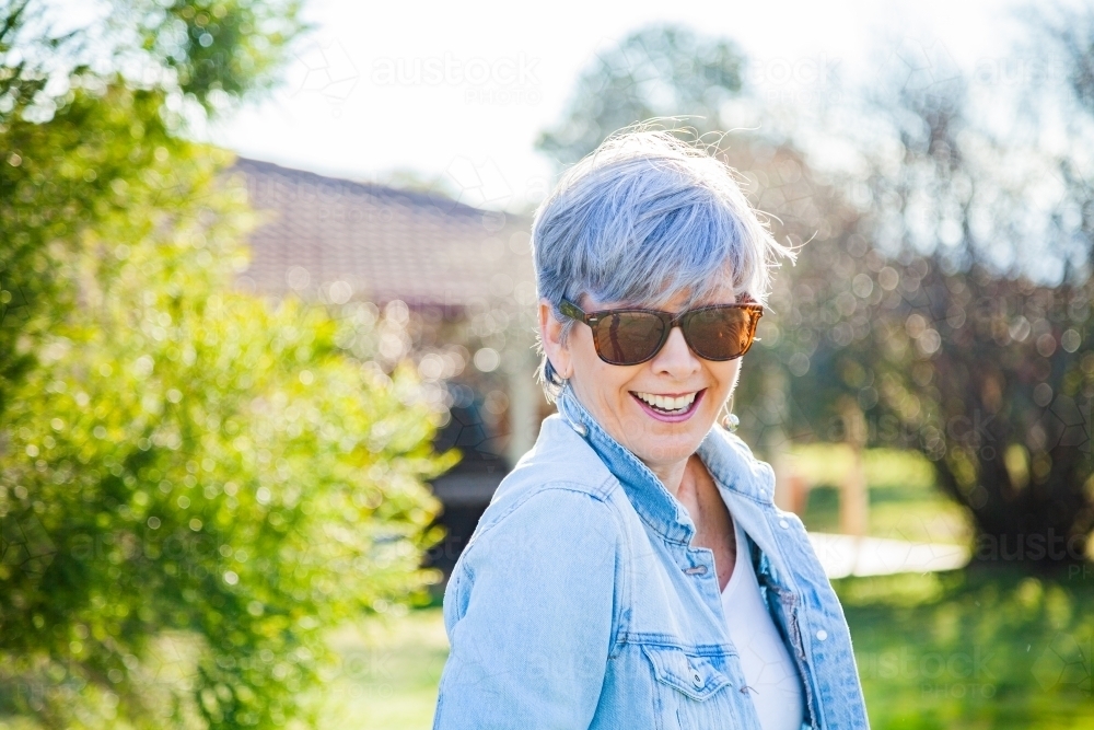 Mature woman in sunnies smiling in the garden - Australian Stock Image