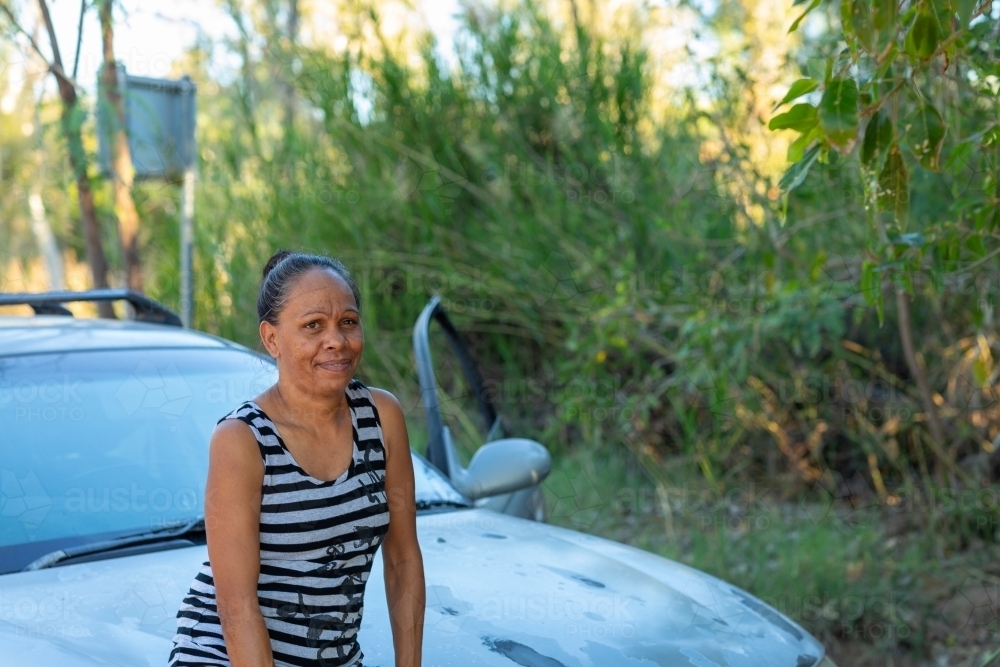 mature woman leaning on car bonnet on roadside - Australian Stock Image