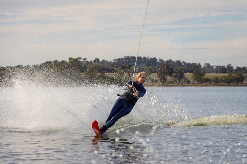 Image of mature woman on single ski waterskiing with water spraying up