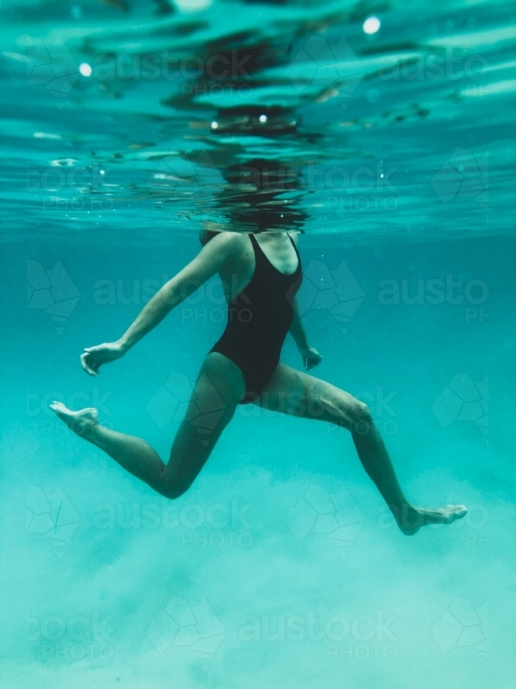Mature woman's athletic body treading water from underwater perspective in ocean - Australian Stock Image