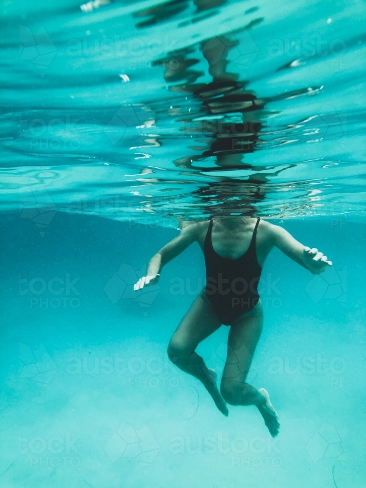 Mature woman's athletic body treading water from underwater perspective in ocean - Australian Stock Image
