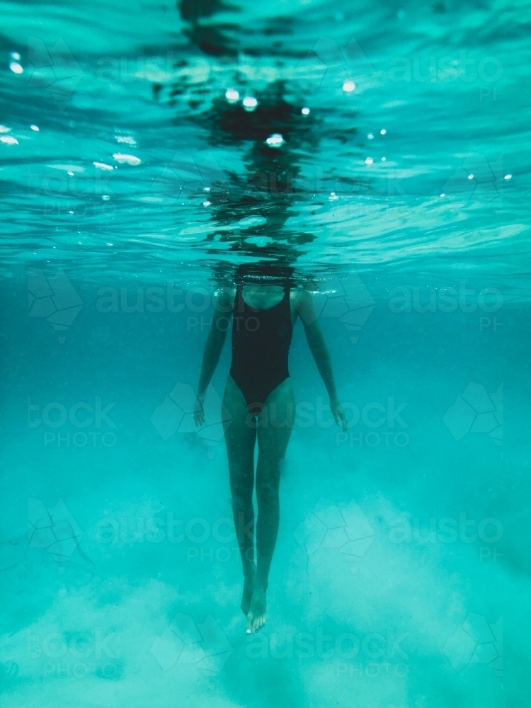 Mature woman's athletic body treading water from underwater perspective in ocean - Australian Stock Image