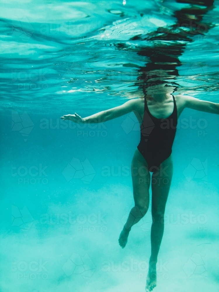 Mature woman's athletic body treading water from underwater perspective in ocean - Australian Stock Image