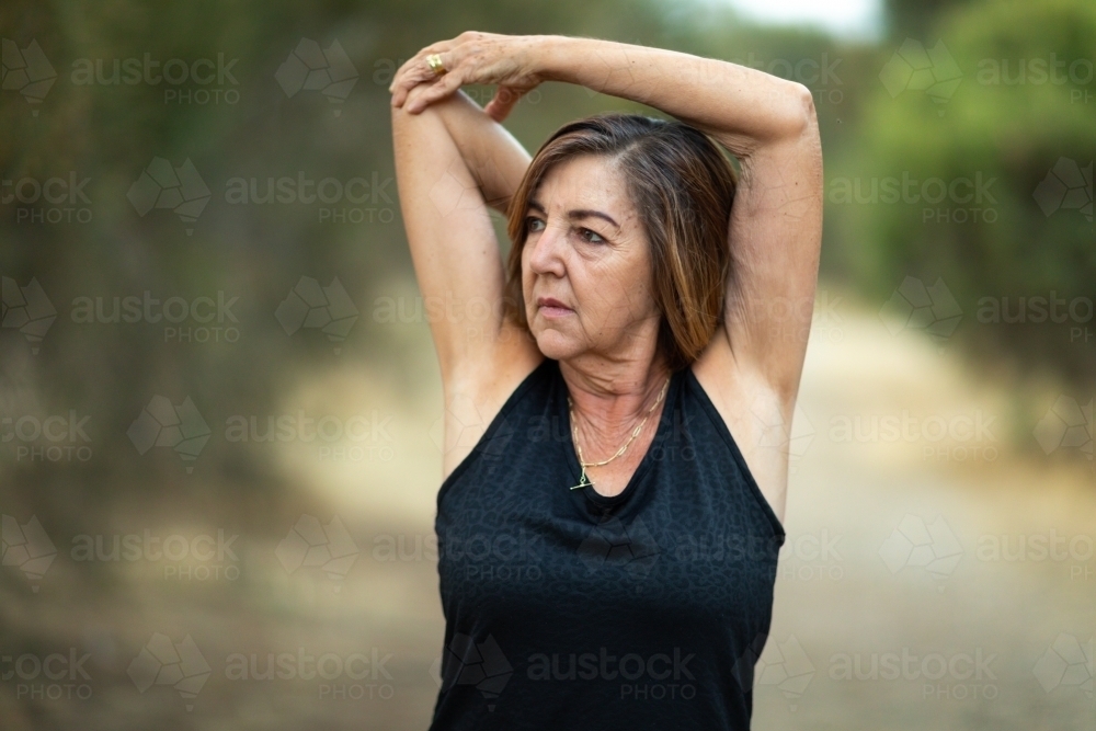 Mature woman with arms above head doing arm and shoulder stretching exercises - Australian Stock Image
