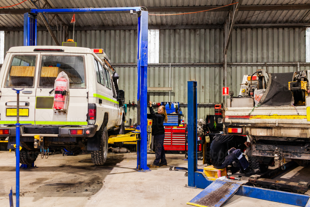 mechanics working on mining fleet vehicles in industrial workshop with cars of lifts - Australian Stock Image