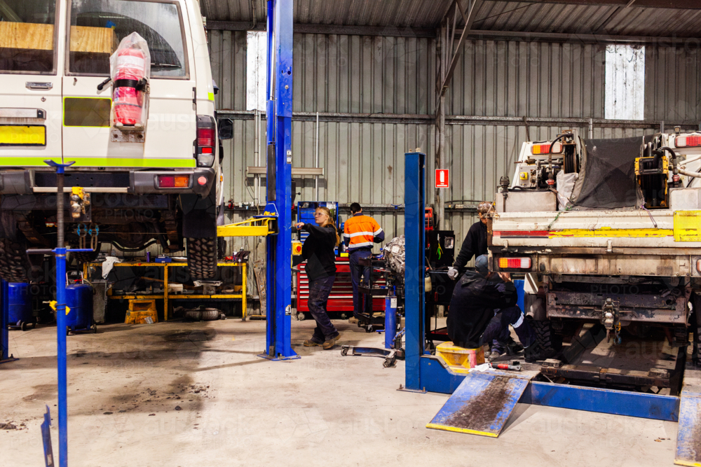 mechanics working on mining fleet vehicles in industrial workshop with cars on lifts - Australian Stock Image