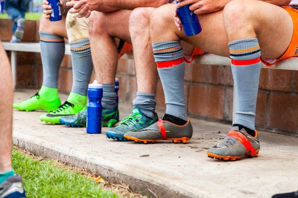 Men in sports shoes sitting on the sidelines of a rugby game - Australian Stock Image