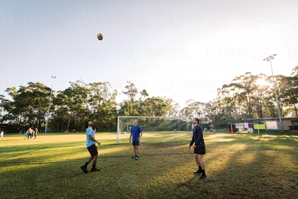 men playing soccer in the field with the ball up in the air on a sunny day - Australian Stock Image