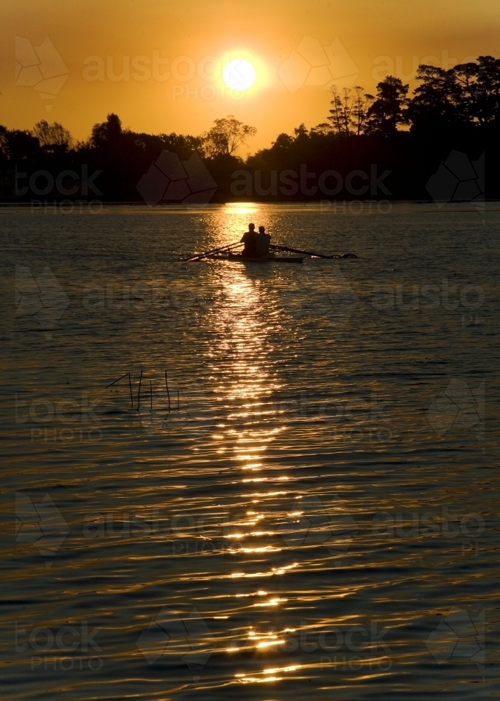 Men rowing on a lake at sunset - Australian Stock Image