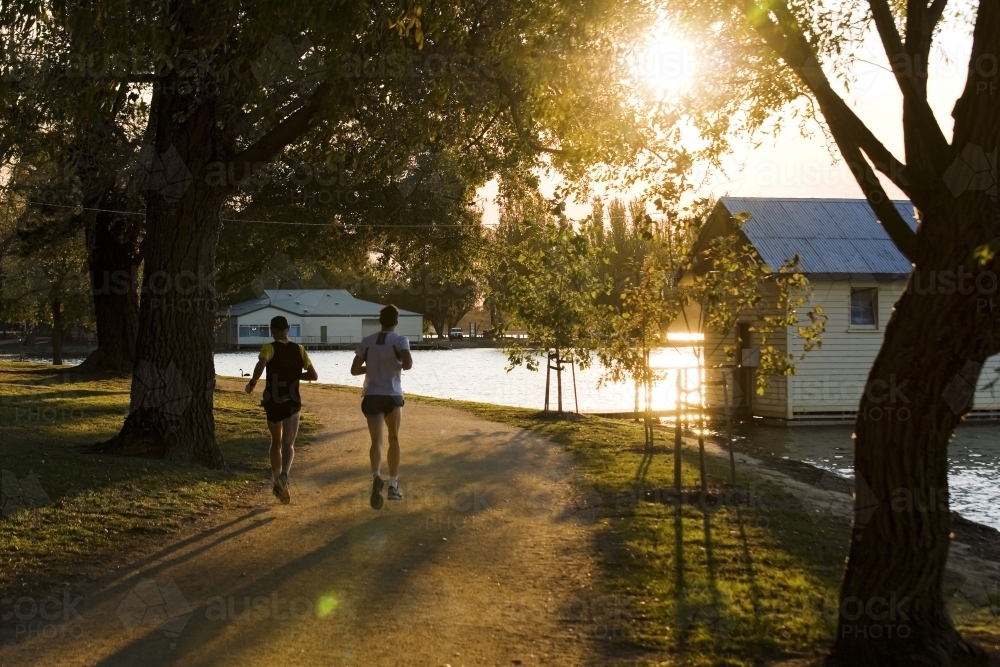 Men running around a lake at sunset - Australian Stock Image