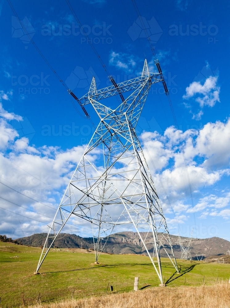 Metal power pole structure with powerlines in sunlight against cloudy blue sky - Australian Stock Image