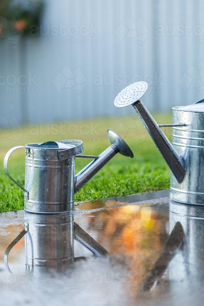 Image of Metal watering cans outside in backyard after rain reflection