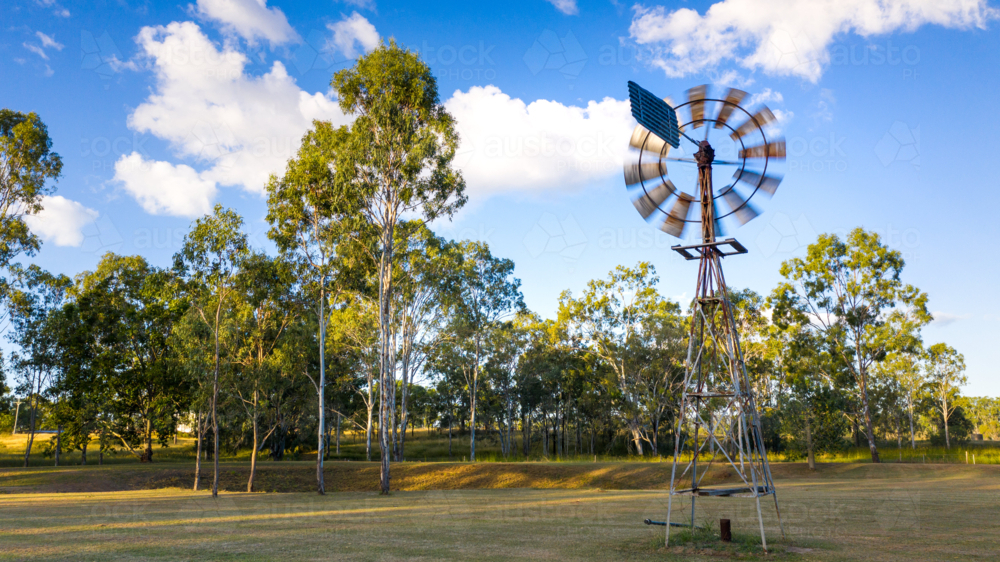 Metal windmill stands prominently in the foreground - Australian Stock Image