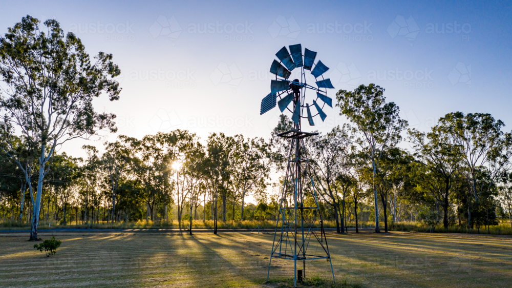 Metal windmill stands prominently in the foreground - Australian Stock Image