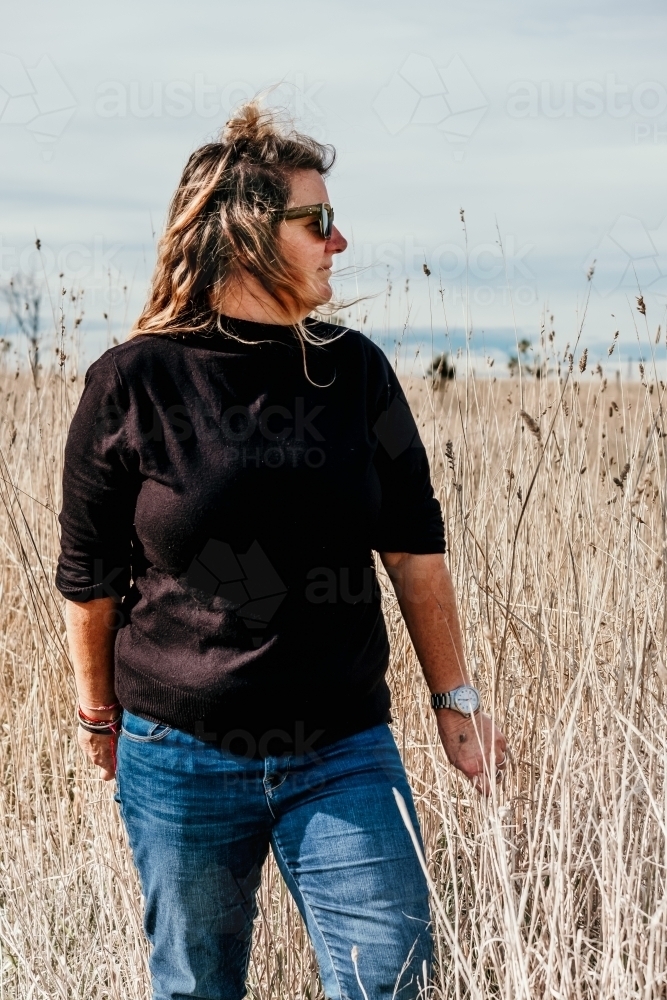 Mid fifties woman in long dry grass. - Australian Stock Image