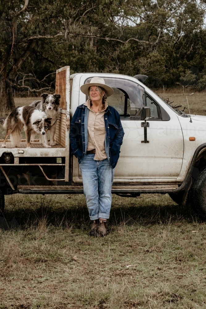 Mid fifties woman with eyes closed stands next to ute on the farm. - Australian Stock Image