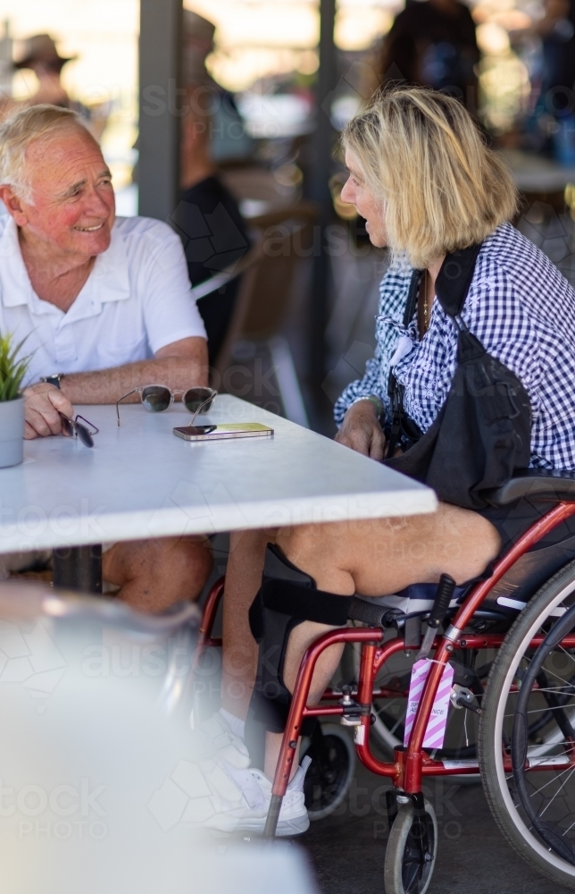 middle-aged couple at cafe table with woman in wheelchair - Australian Stock Image