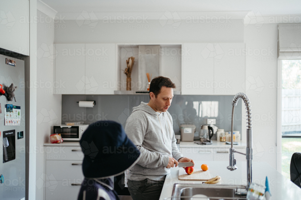 Middle-aged guy cutting fruit for school lunch on the kitchen counter - Australian Stock Image