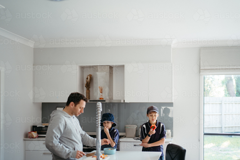 Middle-aged guy cutting fruits on the kitchen counter with the kids. - Australian Stock Image