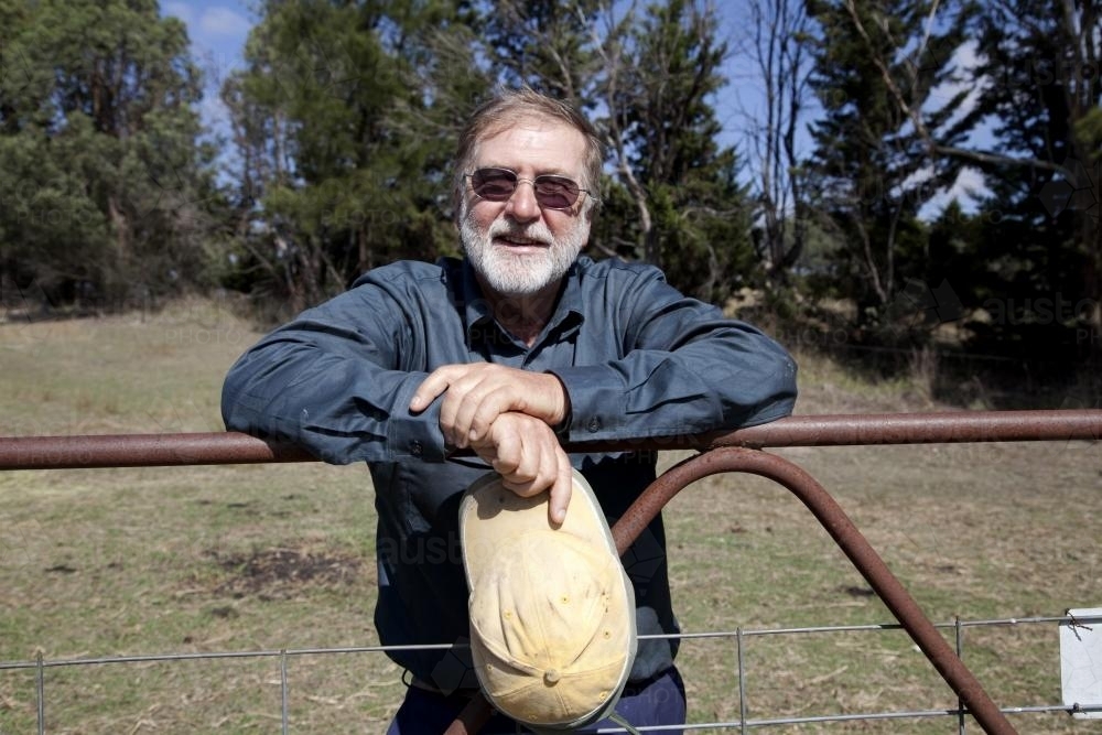 Middle aged male farmer leaning on gate on rural property - Australian Stock Image