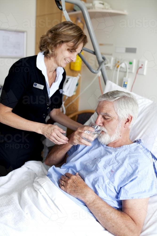 Middle aged male patient being given water by a nurse in a hospital ward - Australian Stock Image