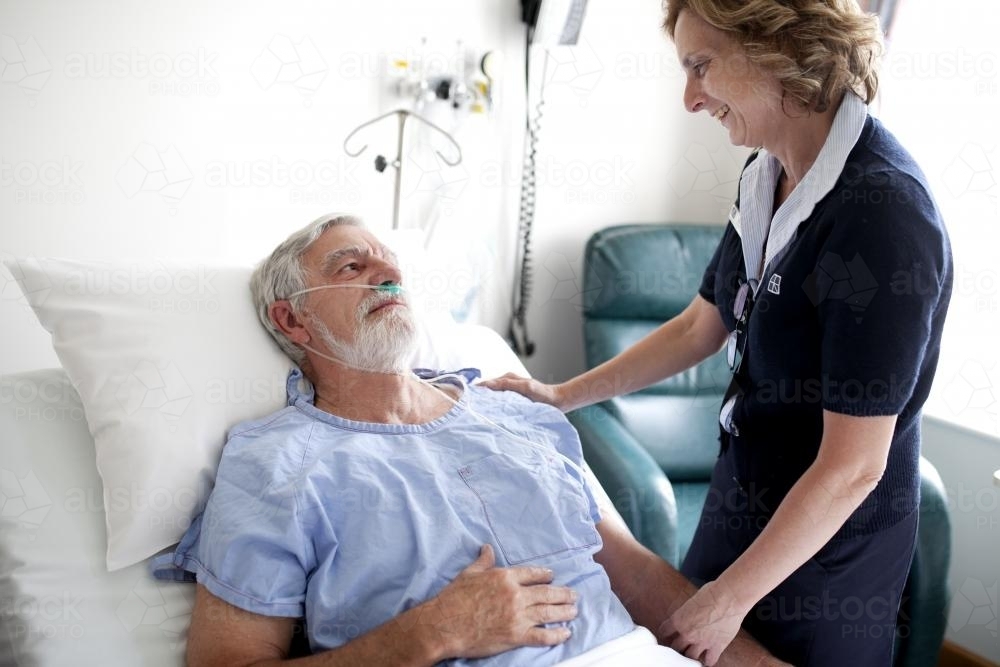 Middle aged male patient talking with a nurse in a hospital ward - Australian Stock Image
