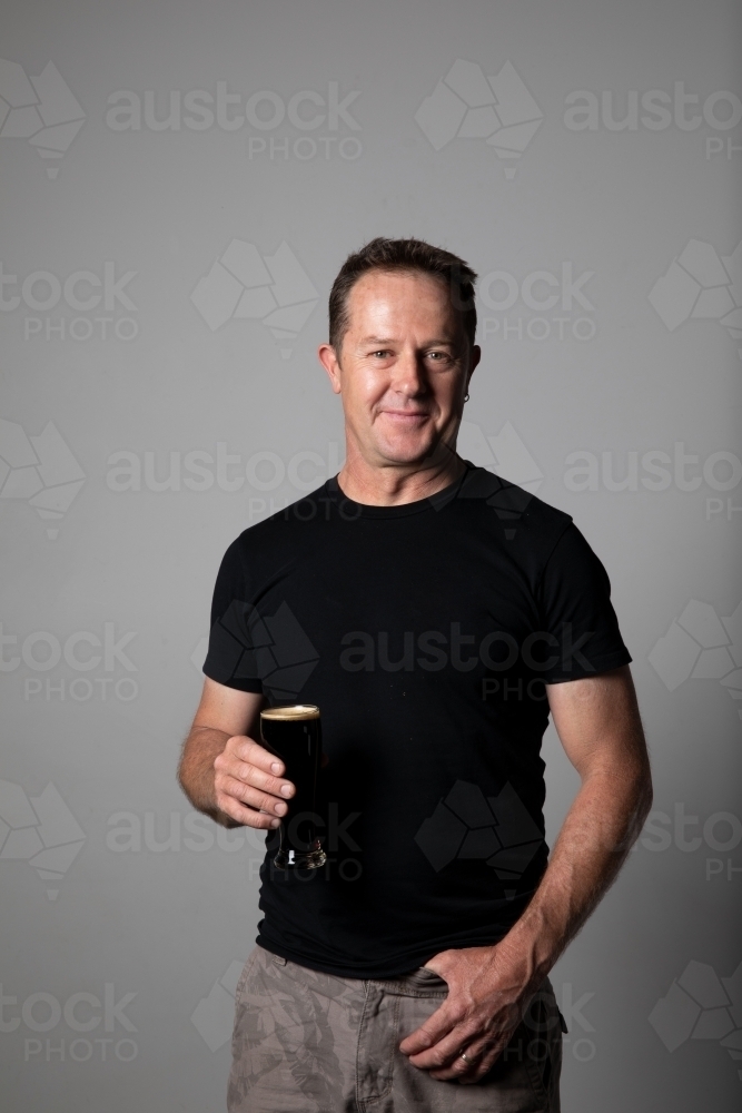 Middle aged Man holding a glass of beer, relaxed and happy - Australian Stock Image