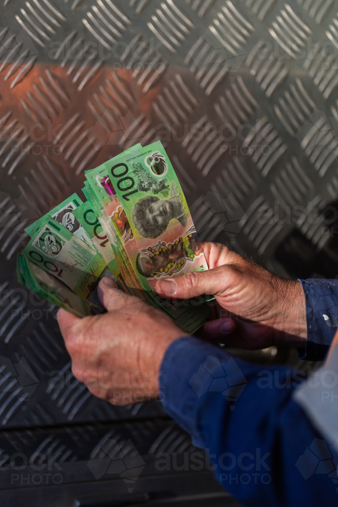 Middle aged man holding hundreds of dollars of Australian cash beside meal tool box on ute - Australian Stock Image