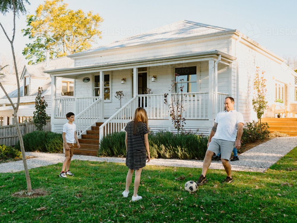 Middle aged man playing soccer with his kids in their front yard. - Australian Stock Image
