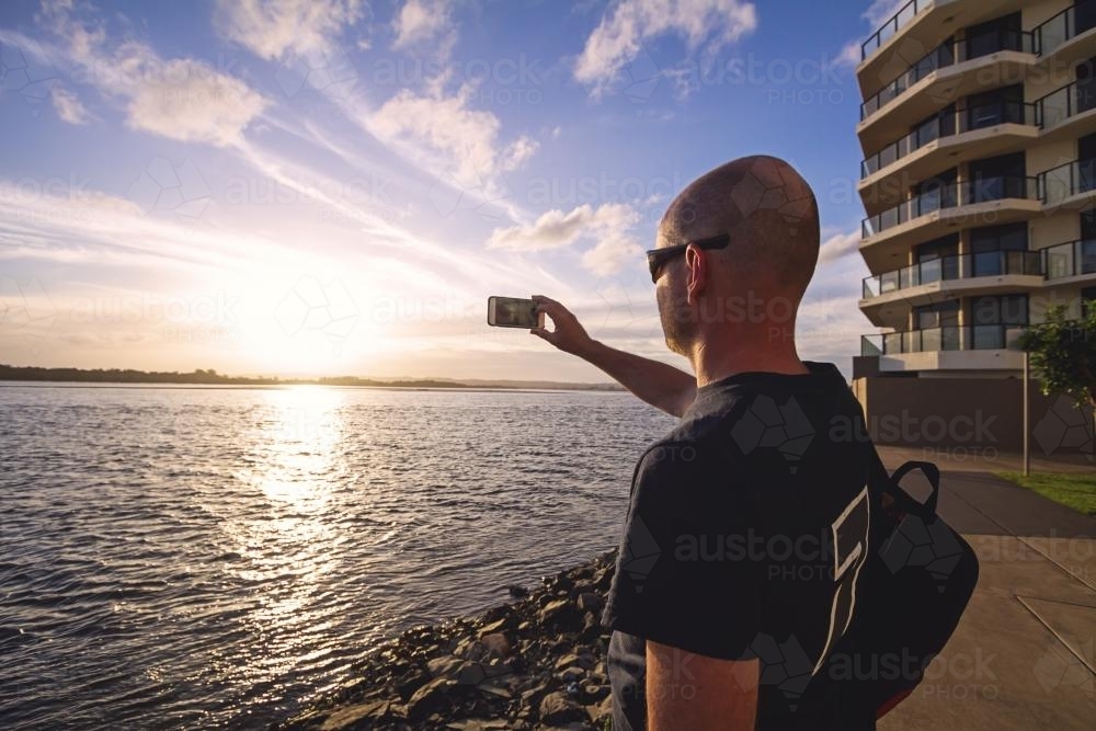 Middle aged man taking a photo with his phone of Richmond River in Ballina, NSW - Australian Stock Image