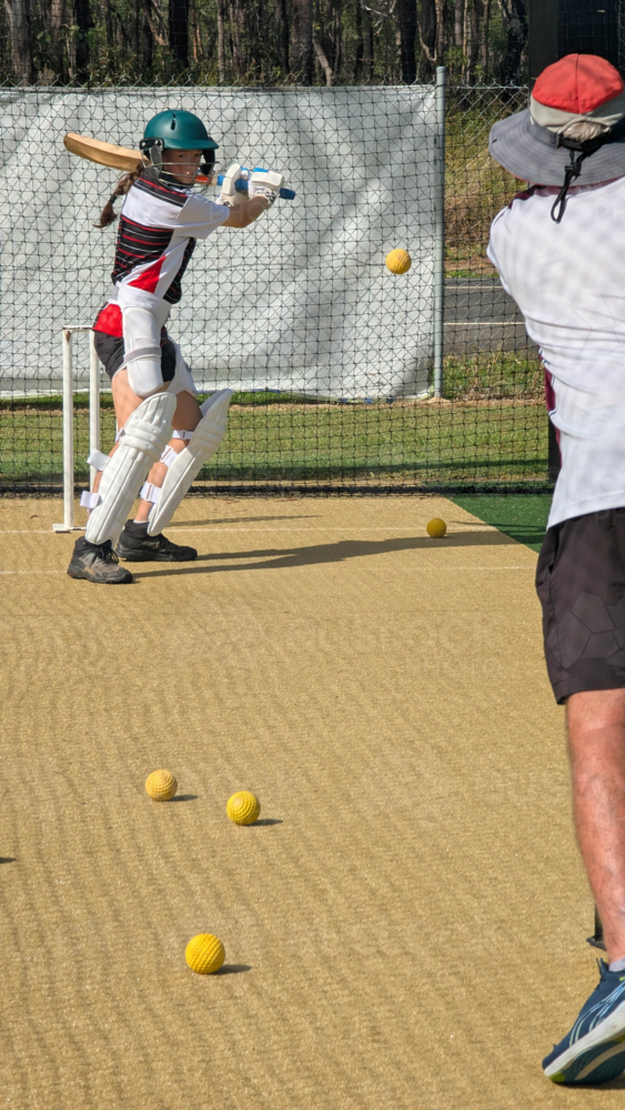 Middle-aged man throwing cricket balls to female batter. - Australian Stock Image