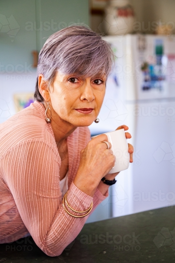 Middle aged woman drinking a cup of tea in her kitchen - Australian Stock Image