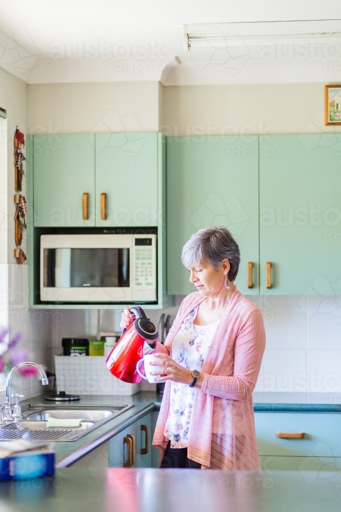 Middle aged woman in her kitchen making a cup of tea - Australian Stock Image
