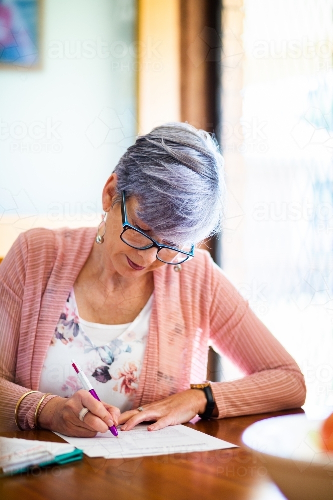 Middle aged woman signing paper documents and forms - Australian Stock Image