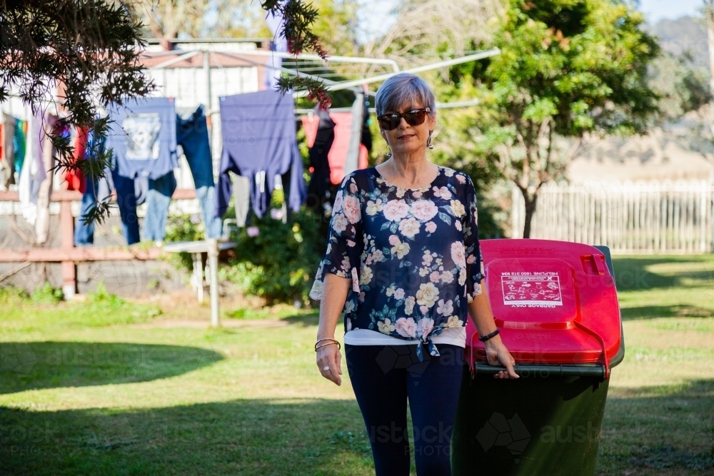 Middle aged woman taking rubbish bin out for collection - Australian Stock Image