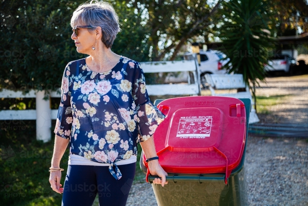 Middle aged woman taking rubbish bin out for collection - Australian Stock Image