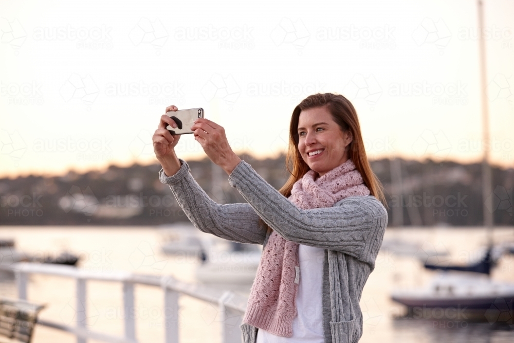 Middle aged woman using mobile phone on wharf to take selfie - Australian Stock Image