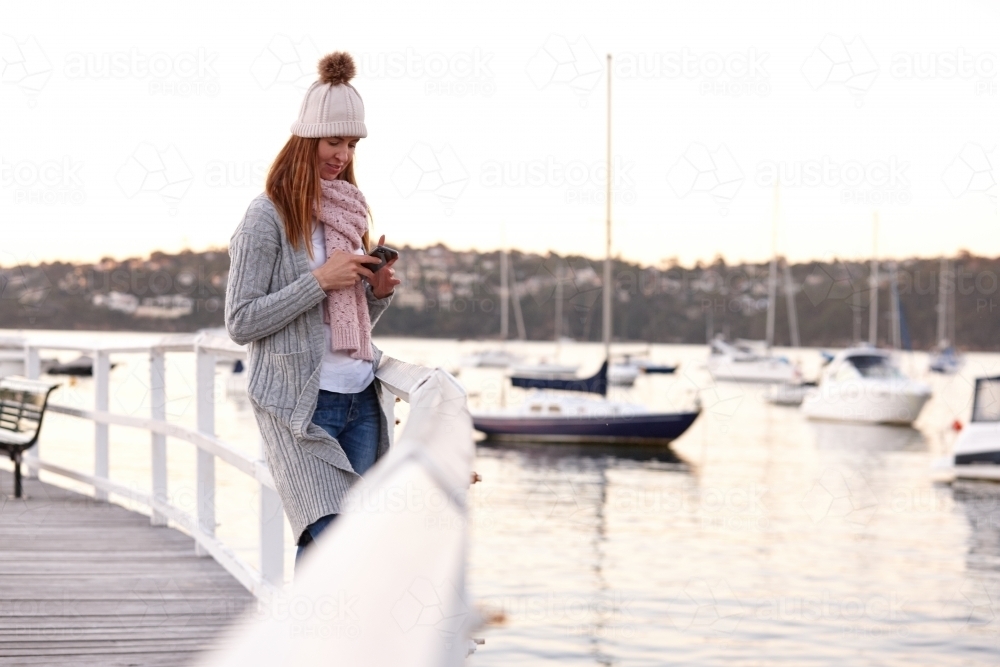 Middle aged woman using mobile phone on wharf wearing beanie - Australian Stock Image