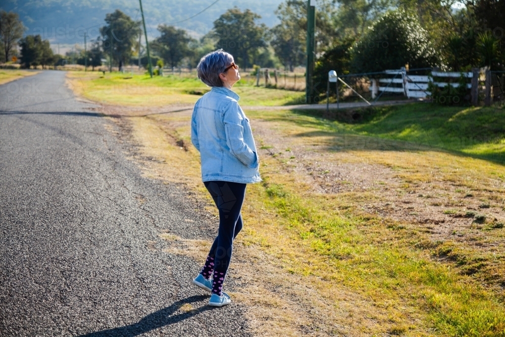 Middle aged woman walking down a rural road for exercise - Australian Stock Image