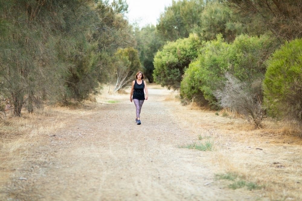 middle-aged woman walking on walking path in bushland setting - Australian Stock Image
