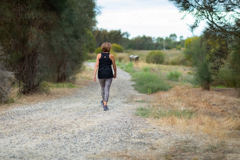 middle-aged woman walking on walking path in bushland setting - Australian Stock Image