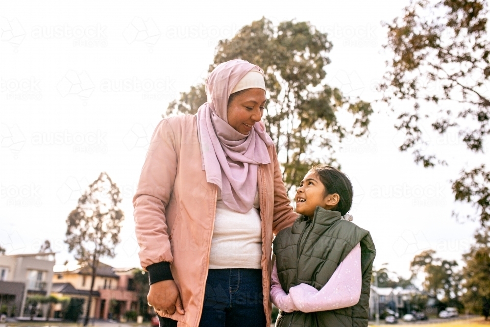 Middle aged woman wearing pink hijab and a girl wearing green coat looking at each other - Australian Stock Image